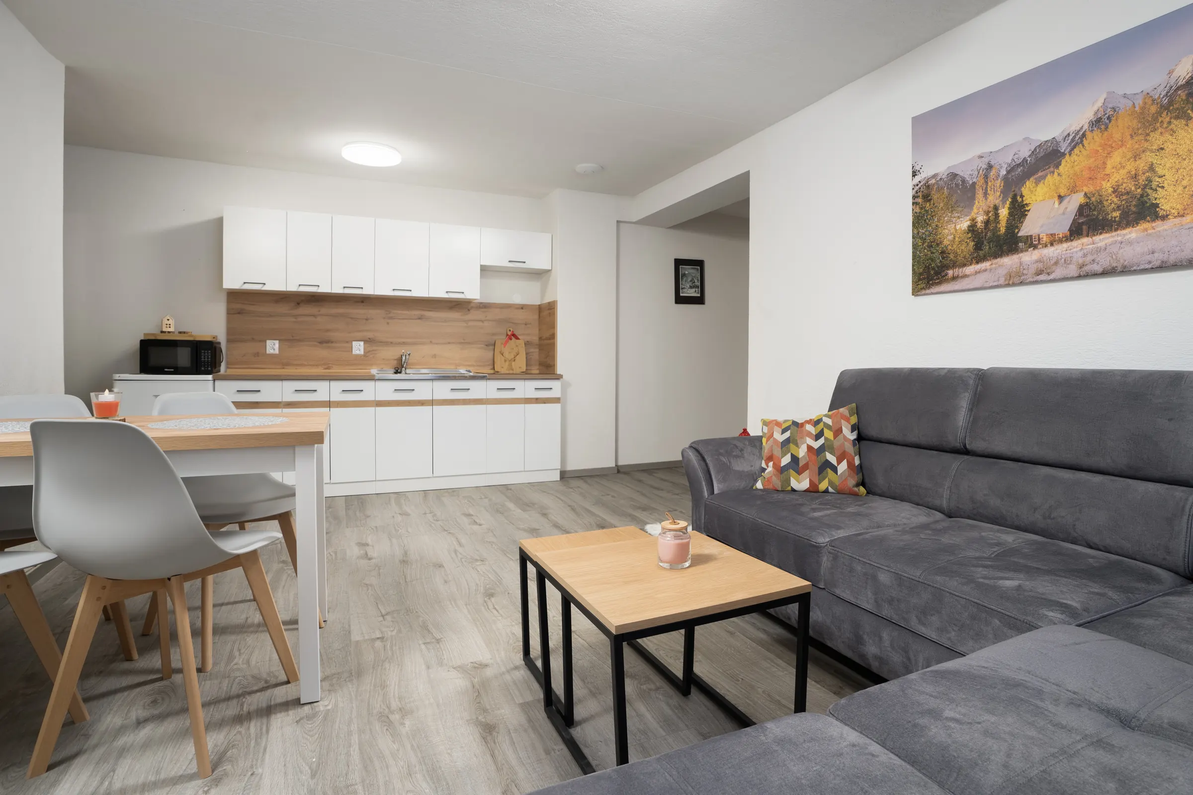 Obývačka s kuchyňou v apartmáne č. 2: biela kuchynská linka, jedálenský stôl a rohová sedačka
