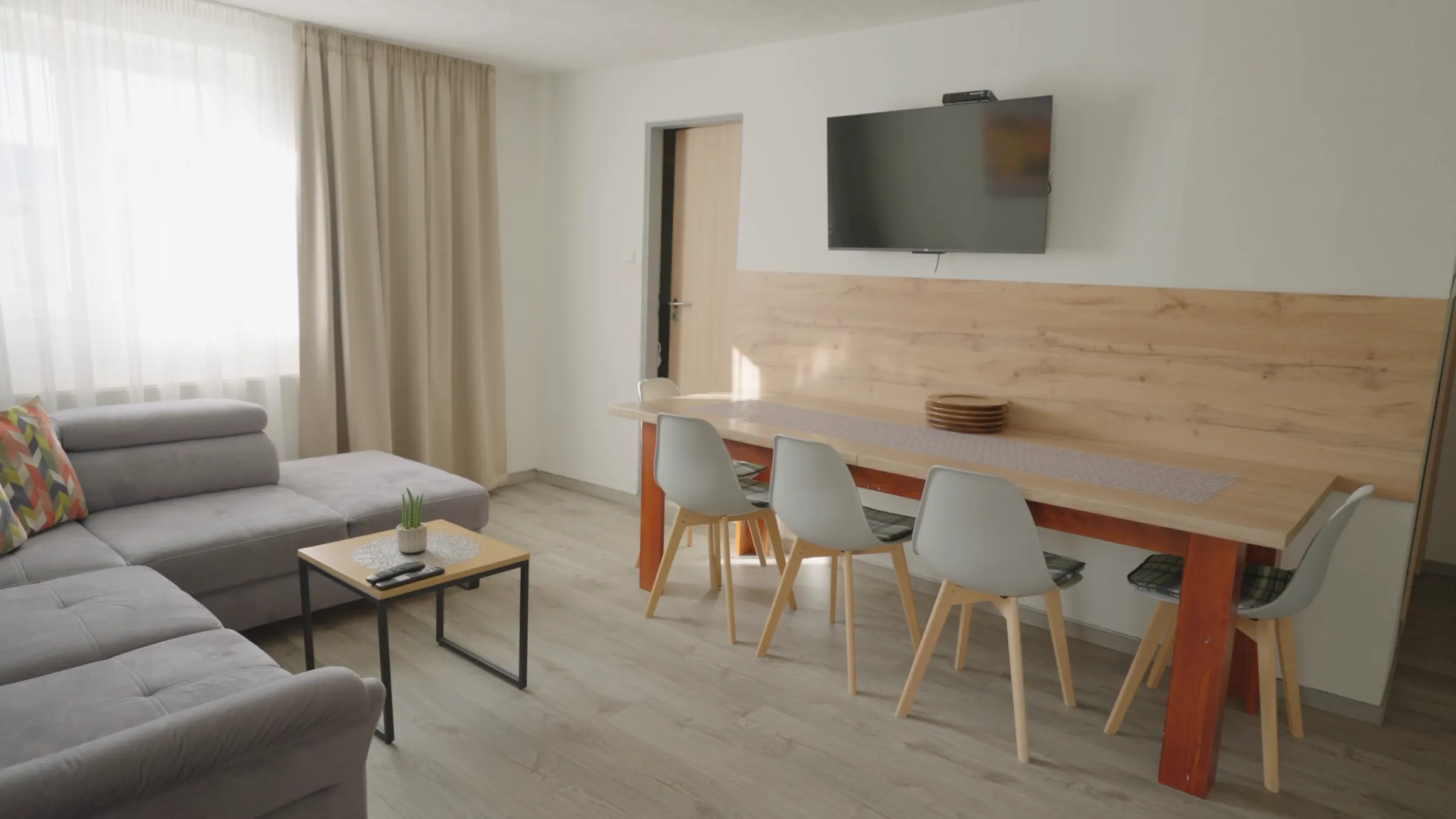 Obývačka apartmánu so sivou sedačkou a televízorom