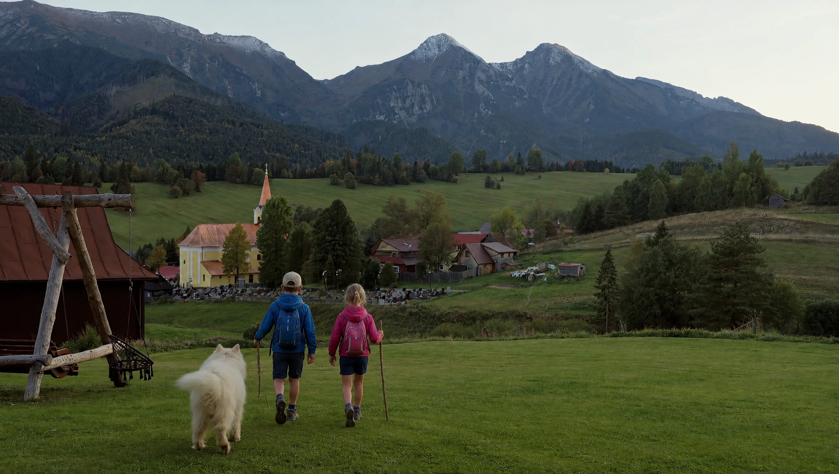 Dve deti s batôžkami a samojed kráčajú po lúke pri dome k Belianskym Tatrám