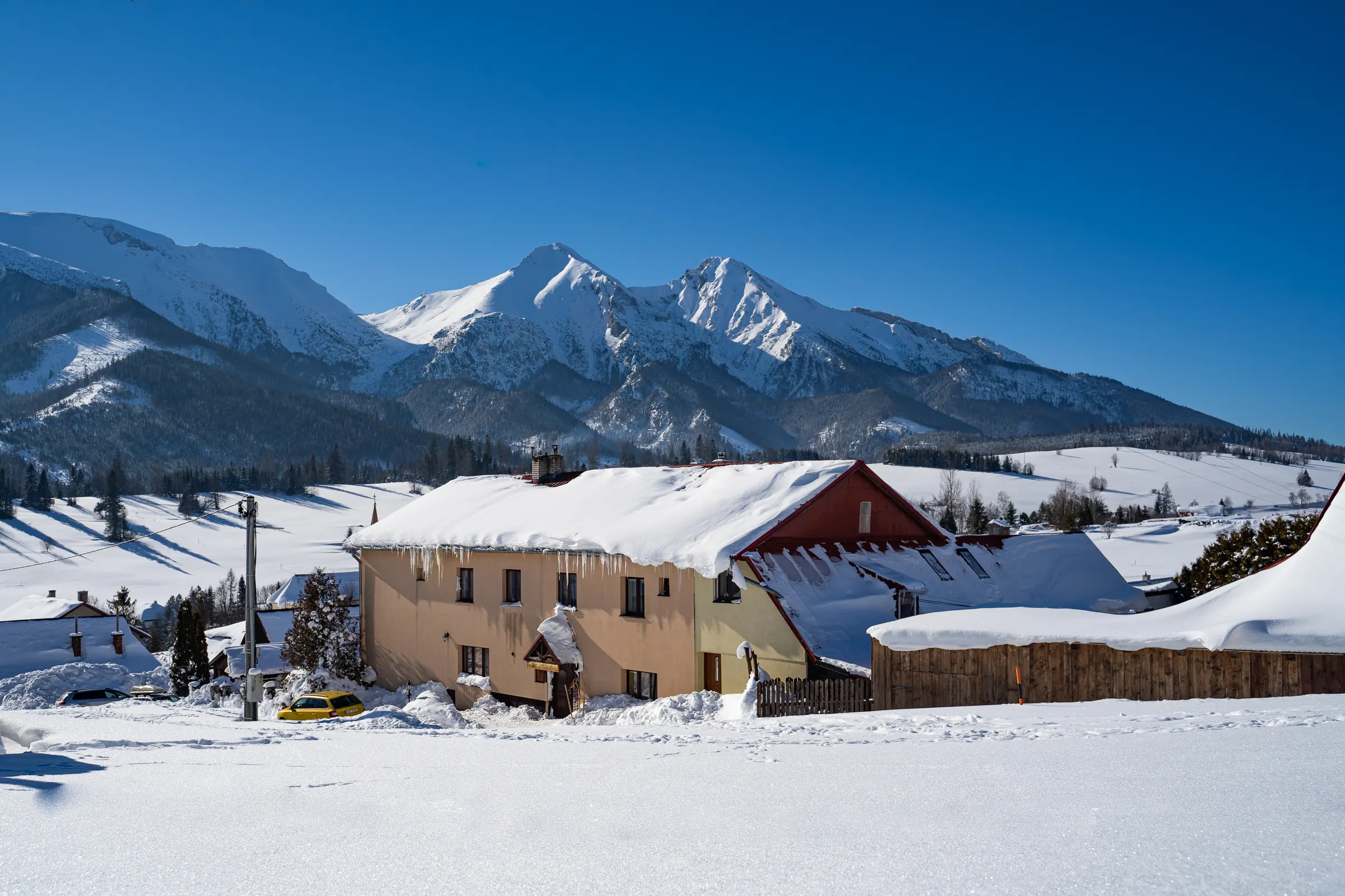 Dom U Maťka a Kubka v zime z kopca, za ním zasnežené Belianske Tatry