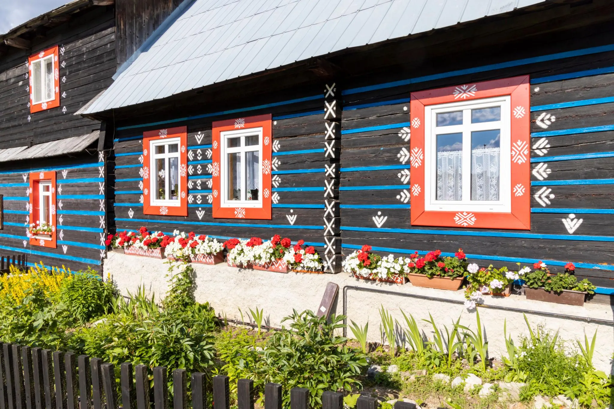 Goral timber house with blue joints, decorated red window frames and geraniums