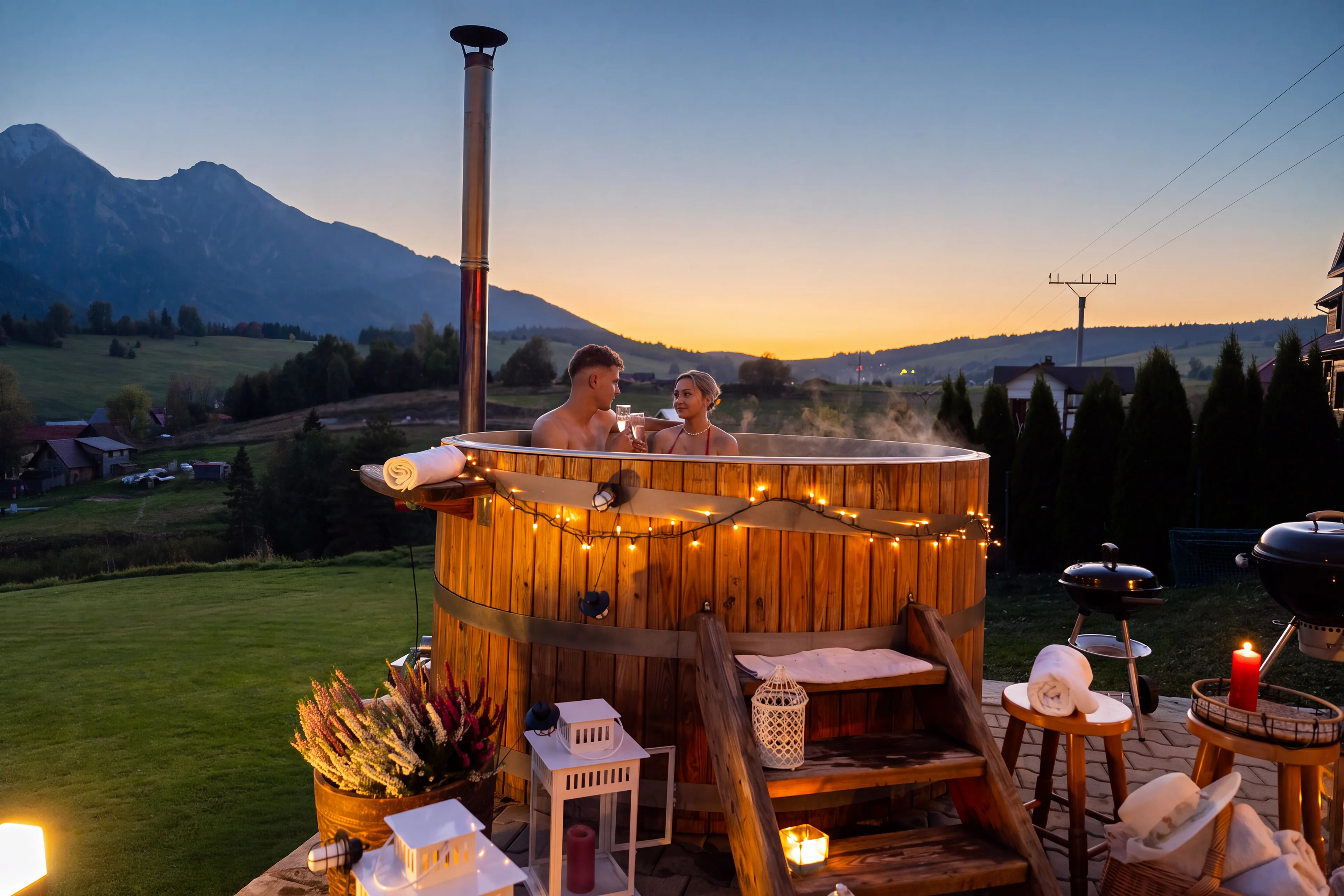 Couple in the wooden hot tub on the terrace at sunset, with the Belianske Tatras behind