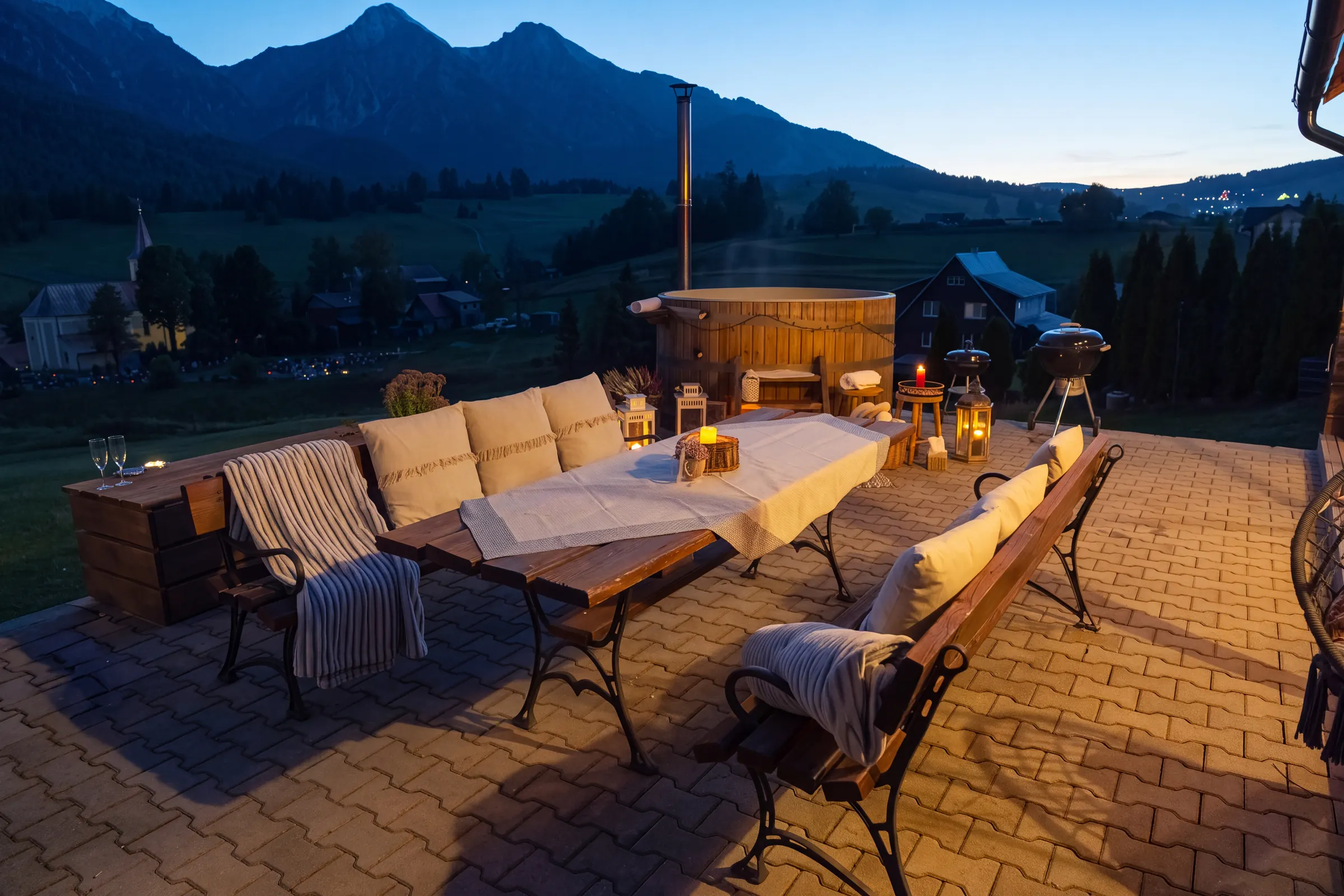 Terrace with a table and benches at dusk, with the hot tub and Belianske Tatras behind