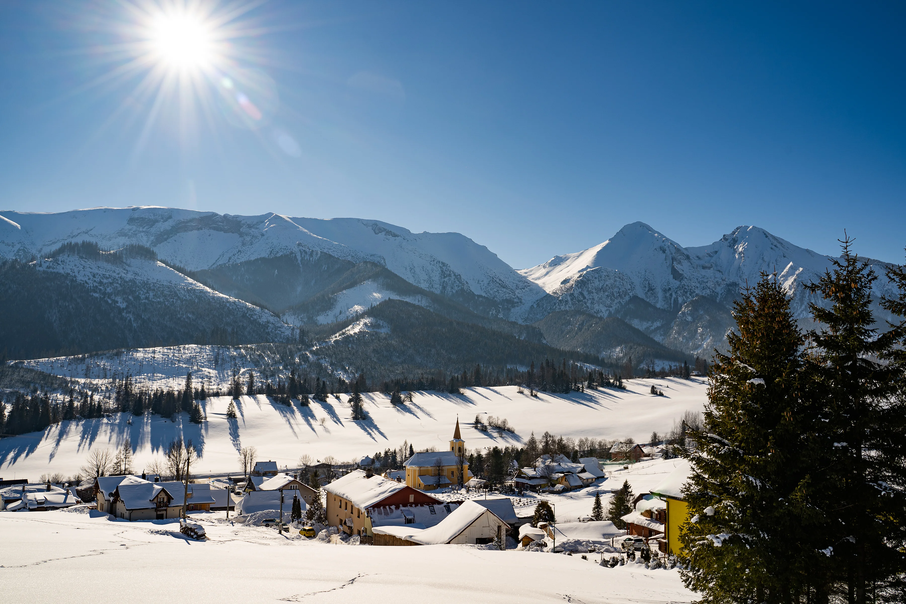 Zasnežený Ždiar s kostolom, nad ním Belianske Tatry a zimné slnko