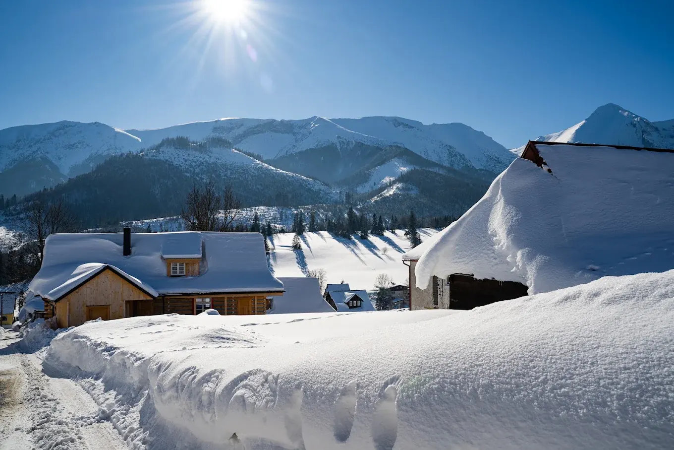 Snowy road in Ždiar, a timber cottage and a house with snow on its roof, with the Belianske Tatras above
