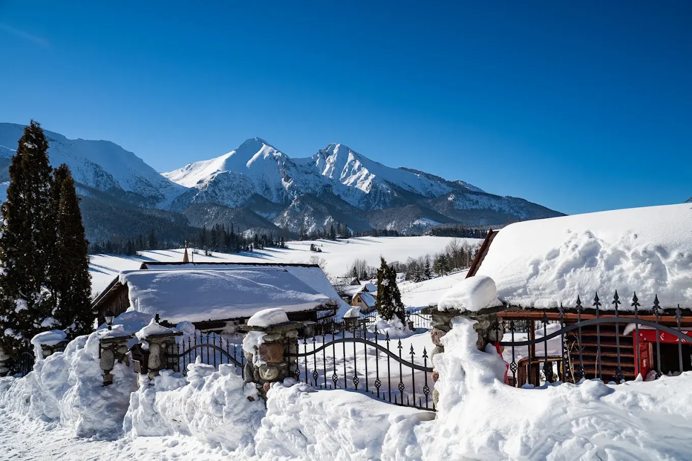 Snow-covered fence with stone pillars, with the Belianske Tatras behind